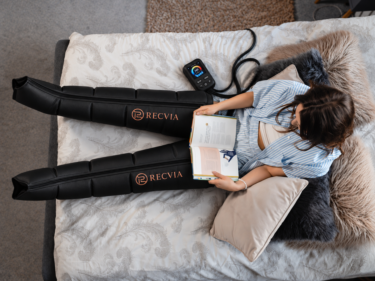 A woman resting on a sofa, wearing RecLegs recovery boots and holding the remote.
